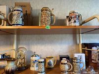 Five small decorative beer steins, a jug, and a small clock arranged on wooden shelves, showing various artistic and relief designs with lids on most steins and vintage clock included.