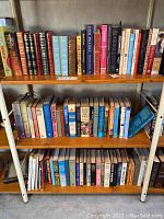 Three shelves of assorted hardcover books including fiction and classic literature, showing spines and titles.