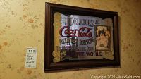 Photo showing full view of the 14x20 inch vintage Coca-Cola mirror with dark brown wooden frame. Mirror text and artwork clearly visible. Wall background visible for scale.