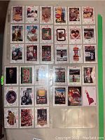 Photo of an album page showing 28 Coca Cola collector cards stored in plastic sleeves, highlighting various vintage advertisements and artwork.
