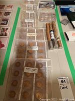 Display of multiple US coins in protective sleeves labeled by year and denomination with proof-like finish, along with rolls of coins and boxed sets visible