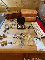 Overview of jewelry pieces arranged on counter including necklaces, earrings, pins, and two jewelry boxes visible in background.