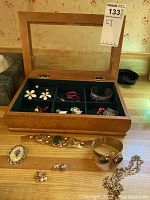 Wooden jewelry box containing various jewelry items including earrings, rings, bracelets, and brooches, set on a wooden surface