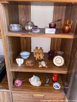 Photo of wooden shelves with small figurines, glass items, and decorative pieces including a candle holder and orange vase