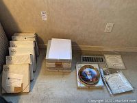 14 decorative plates stacked and arranged beside their boxes and certificates of authenticity on floor