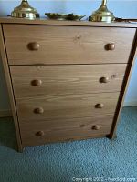 Front view of a wooden dresser with four drawers, each with two round wooden knobs, showing natural wood grain and finish.
