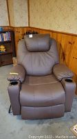 Front view of brown motorized faux leather recliner showing built-in cup holders on both armrests and plush padded cushions.