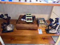 Shelf display with wooden chess board topped with electronic chess timer and boxed puzzles. Flanked by two metal bookends on either side.