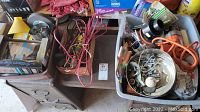 Wide view showing several boxes and containers with mixed hardware, tools and electrical cords on and beside a wooden chest