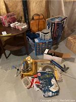 Wide view of lot showing model kit, hardware boxes, tools, and other items arranged on basement floor and table.