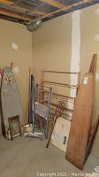 Photo of a laundry corner showing two wooden vintage ironing boards, several drying racks including a copper-colored metal rack and folding metal rack, and a Pearl washboard leaning against the wall.