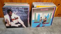 Two stacks of vinyl LP records featuring various rock and R&B albums including prominent artists Billy Ocean and Ella & Louis.