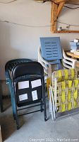 Photo showing a stack of various outdoor lawn chairs including a black metal folding chair, green molded plastic chair, white molded plastic chair, a blue slatted backrest chair, and foldable lawn chair with yellow and white woven straps.