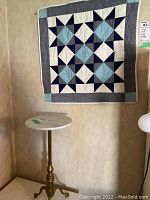 Photo showing the small round table with metal stand and white stone top below the quilt wall hanging