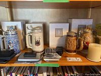 Wide shot showing four beer steins, three calculators stacked and spaced apart, and one candle on shelf