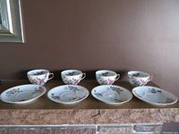 Front view of the set showing four porcelain teacups and matching saucers on display, arranged in a row.