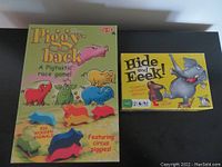 Two boxed children's games: Piggy Back Race and Hide and Eek! laid flat on table.