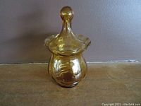 Front view of amber covered candy dish showing ribbed body and ruffled lid edge with knob handle.