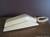 Side angle view of the yellow rotary phone showing the handset and base, coiled cord visible.