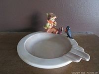 Front view of cream-colored ashtray with seated boy figurine and bird.