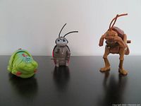 Three wind-up toys from Pixar's A Bug's Life displayed on a black surface with a white background, showing Hopper, Francis Ladybug, and Heimlich Caterpillar side by side.