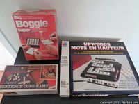 Photo of three boxed vintage word games: Big Boggle in red box, Scrabble Sentence Cube Game in dark box with light cover, and Upwords in large box with French and English text on cover.