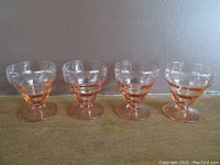 Four pink depression glass dessert glasses arranged in a row, showing ribbed texture with four horizontal rings around the bowl.