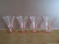 Four pink depression glass parfait goblets arranged in a row, showing the overall shape and color.