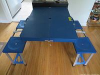 Blue portable children's picnic table fully set up showing four attached seats around the table on a hardwood floor.