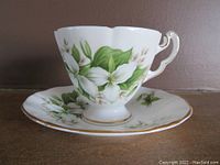Teacup showing white trillium flowers with green leaves and gold-trimmed scalloped edge and handle.