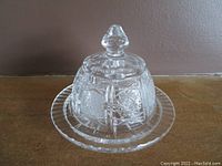 Clear cut glass covered butter dish with intricate patterns, knobbed lid, and round base plate