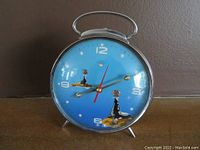 Front view of vintage blue dial Shanghai mechanical alarm clock with two seal illustrations and metal body with chrome finish.