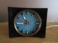 Front view of the Westclox vintage plug-in clock showing black square case with curved front and blue face with hour markers and hands.