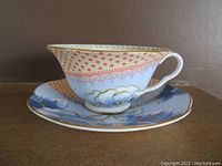 Side angle view of Wedgwood Butterfly Bloom blue peonies teacup and saucer on wooden surface, highlighting the cup's shape and patterns.