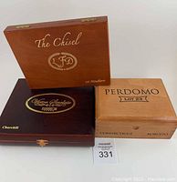 Three wooden cigar boxes stacked together; largest Perdomo box on top with visible dovetail joints, medium Chisel LFD box underneath, and dark Victor Sinclair Churchill box at bottom.