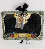 Top view of rectangular metal magnetic memo board with butterfly and floral decorations, magnets attached in bag, and black ribbon hanger.
