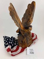 Front and side view of the hand carved wooden eagle with wings spread upward, sitting on an American flag scarf.