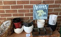 Photo showing an arrangement of various ceramic orchid planters, the copper herb pots set, the moss basket, and the flower sign hanging on a brick wall.