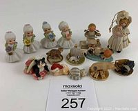 Full view of all 14 miniature figurines including spaghetti collared girls, animal figurines, Jan Hagara doll, and wooden girl with scissors.