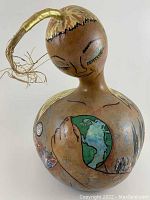Full view of carved and painted gourd figure with Earth on chest and straw-topped head.