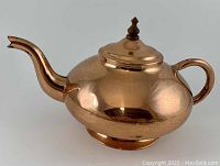 Side view of shiny copper gooseneck teapot with curved spout and handle, showing the genie-shaped body and lid with finial