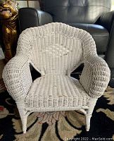 Front view of vintage child's white wicker chair, showing woven texture and scalloped backrest design.