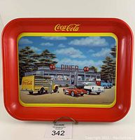 Full view of the red metal Coca Cola tray featuring a diner and classic cars, signature and dated 1991 visible.