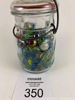 Front side view of the clear glass Ball Ideal jar filled with assorted old marbles, showing bail top metal closure and embossed text.