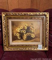 Full view of the framed oil painting showing daisies in a pot, with a heavy ornate gold gilded frame.