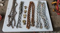 Top-down photo showing all four chains and five hooks laid out on a table, displaying rust and different finishes on chains and hooks.