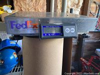 Full view of metal FedEx branded digital scale showing digital display and control buttons.