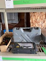 Photo of Stanley drill bit set black case with label, and Maximum grey case behind it, on metal shelving in garage.