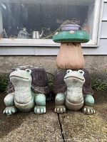 Two frog statues each with turtle shells on their backs placed side by side outdoors.