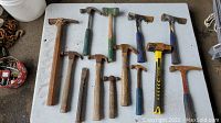 Table with 11 hammers, mallets, axes and a large spike tool, all showing surface rust and use marks.